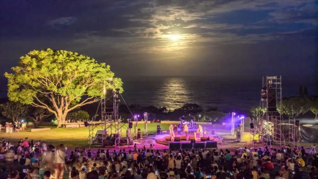 月光海音樂會夜間登場,海邊舞台前聚集觀眾,滿月與月光倒映在遠方海面上。