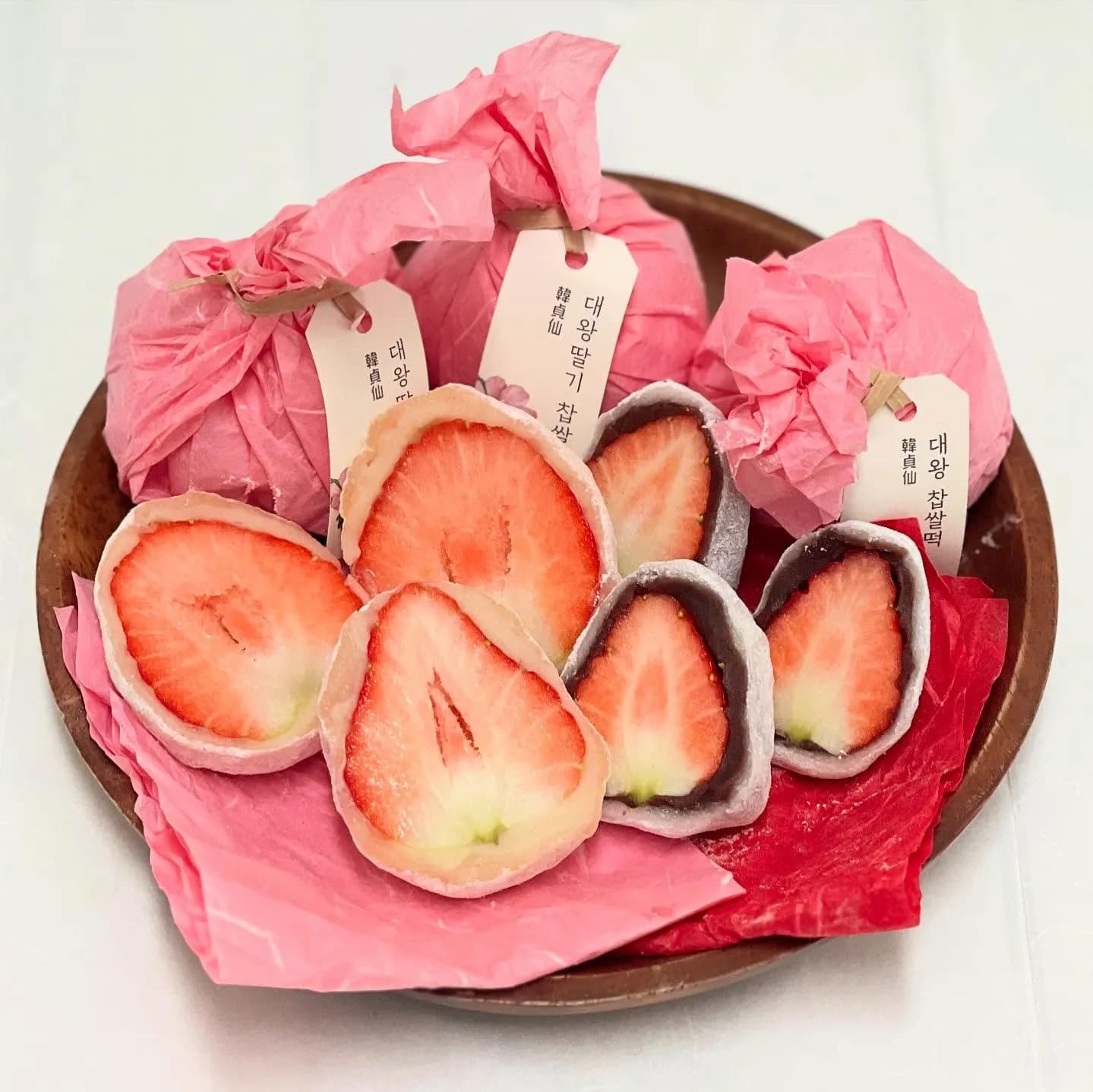 聖水洞甜點名店「韓貞仙」招牌大王草莓大福,以粉色福袋紙包裹,切開展示裹著紅豆與白豆沙的整顆飽滿爆汁鮮草莓。