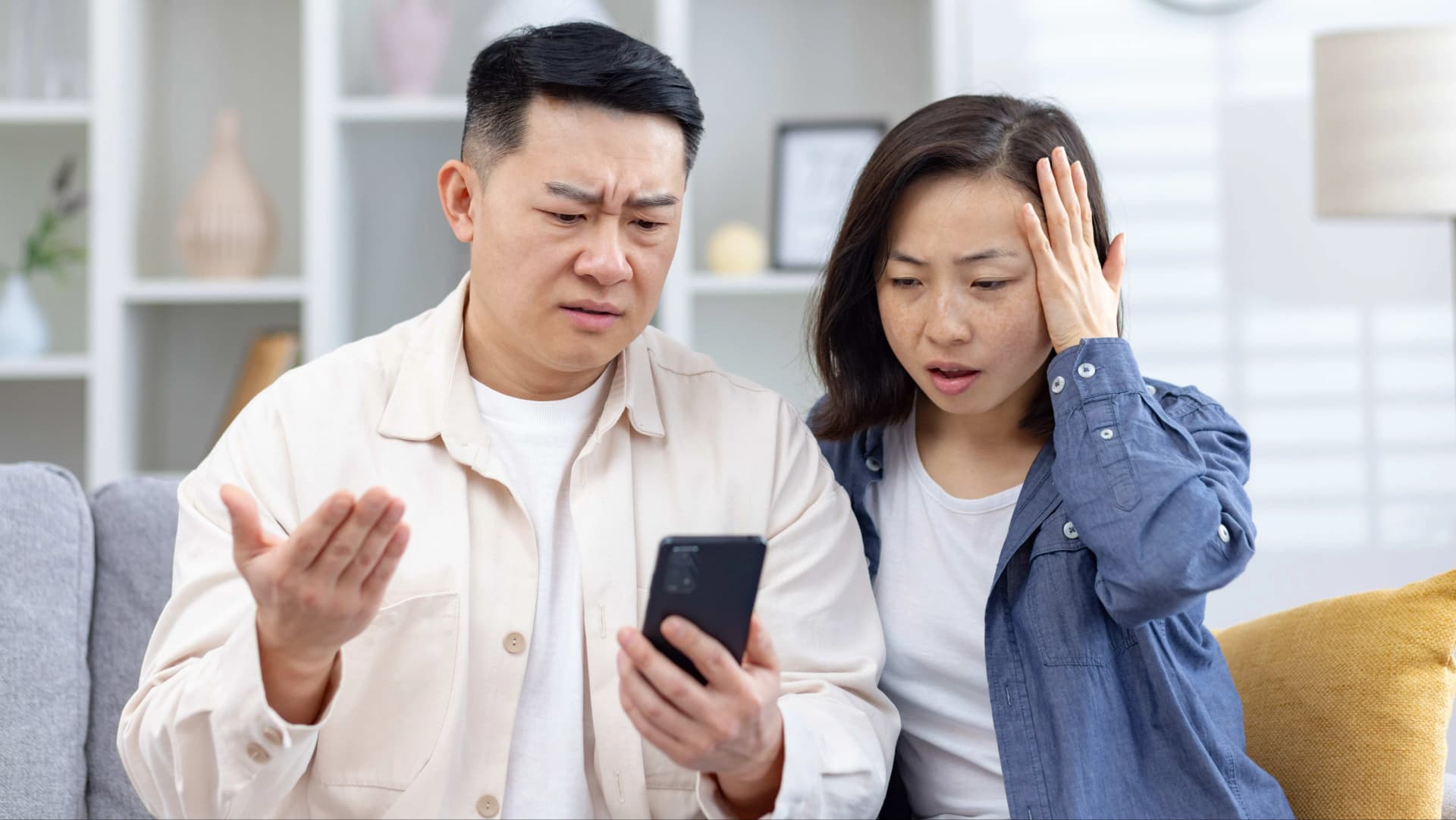 一男一女擔憂地看著手機螢幕。身穿淺色襯衫的男子一邊做著手勢,一邊看著手機;身穿藍色襯衫的女子表情焦慮,撫摸著額頭。
