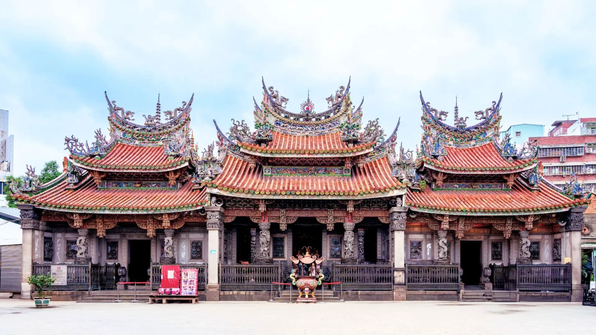 三峽清水祖師廟宏偉的傳統廟宇建築全景,展現精緻的剪黏燕尾屋頂與繁複的石雕神柱,中央擺放著香爐,前方為寬闊的廟前廣場。