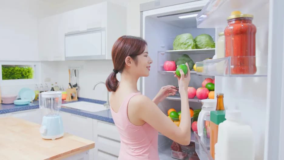 女性開啟冰箱拿取新鮮蔬果,內部擺滿各式蔬果與醬料,展現食材保鮮與靈活收納空間。